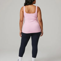 Female model from behind in a studio wearing a pink sleeveless activewear tank top.
