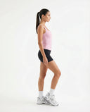 Lifestyle shot of a woman stretching in a sunlit studio wearing a pink sleeveless tank top during a yoga session.
