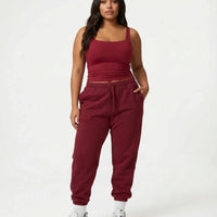 Female model standing front-on in studio wearing red sleeveless crop tank top with matching red joggers and white sneakers.