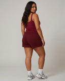Female model standing with back to camera in studio wearing red sleeveless tank top showing back fit and strap detail.