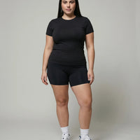 Female model standing front-on in a studio wearing the black crew neck t-shirt top paired with black bike shorts and white sneakers.