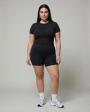 Female model standing front-on in a studio wearing the black crew neck t-shirt top paired with black bike shorts and white sneakers.