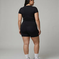 Female model facing away in a studio showing the back fit of the black short sleeve t-shirt top.