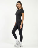 Lifestyle shot of a woman in the black crew neck t-shirt top walking outdoors with coffee, styled with bike shorts and sneakers.