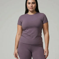 Model standing front-on in studio wearing purple fitted t-shirt top and matching leggings with white sneakers.
