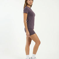 Lifestyle shot of woman stretching in purple fitted t-shirt top during a pilates class in natural light.