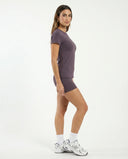 Lifestyle shot of woman stretching in purple fitted t-shirt top during a pilates class in natural light.