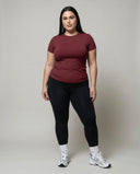 Female model standing front-on in studio wearing red fitted crew neck tee with black leggings and sneakers.