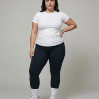 Female model facing forward in studio wearing white ribbed compression t-shirt top with high waist bottoms.