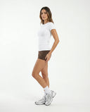 Lifestyle image of woman wearing white ribbed t-shirt top during a casual outdoor walk in natural light.