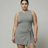 Model wearing grey sculpting sleeveless top and wrap-tie active skirt, front studio view with white sneakers.