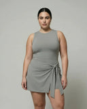 Model wearing grey sculpting sleeveless top and wrap-tie active skirt, front studio view with white sneakers.