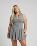 Model wearing SEEN Essential grey padel dress in front-facing studio shot with New Balance sneakers and white socks.