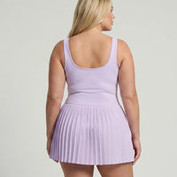 Lifestyle shot of woman in the SEEN Essential purple pleated tennis dress mid-movement highlighting skirt flow and active versatility.