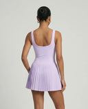 Lifestyle shot of woman in the SEEN Essential purple pleated tennis dress mid-movement highlighting skirt flow and active versatility.