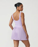 Lifestyle shot of woman in the SEEN Essential purple pleated tennis dress mid-movement highlighting skirt flow and active versatility.