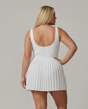 Side profile view of a model wearing the SEEN Essential white tennis dress showing the fitted silhouette and pleated skirt flow.