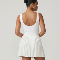 Model wearing the SEEN Essential white tennis dress, back studio view showing supportive wide straps and pleated skirt.