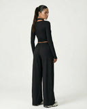 Back view of women's black yoga set featuring a long-sleeve wrap top with tie waist and wide leg pants displayed on the model.