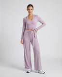 Women's purple yoga set with long-sleeve wrap crop top and wide leg pants displayed on ghost mannequin, front view.