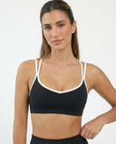 Front view of a black sports bra with white contrast trim and strappy back design, featuring double shoulder straps and sculpting compression fit.
