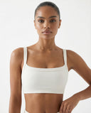 Model wearing a cream ribbed square neck sports bra crop top with wide straps and compression fit, styled against a white background.
