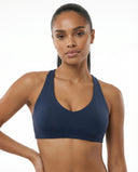 Woman wearing a navy seamless racerback sports bra with sculpting compression fit and deep scoop neckline, front view against a white background.