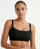 Model wearing a black ribbed square neck sports bra crop top with wide straps and sculpting compression fit against a white background.