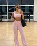 Gym mirror selfie of model wearing pink high waist crossover wide leg leggings with matching sports bra and black bag